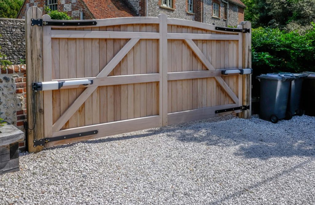 Tall large wooden entry electric gates which are closed. Looking from the inside with a stone driveway in the foreground